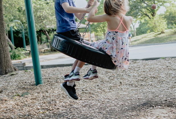 Zwei Kinder sitzen auf einer Reifenschaukel auf einem Spielplatz.