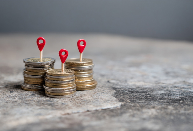 Einige Stapel mit Euro-Münzen, aus denen kleine rote Positionsnadeln rausstechen.