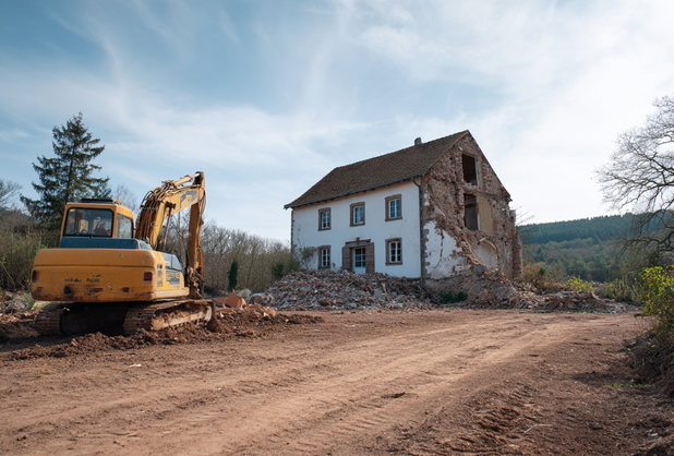 Ein halb abgerissenes Haus und ein Bagger auf einer Baustelle.