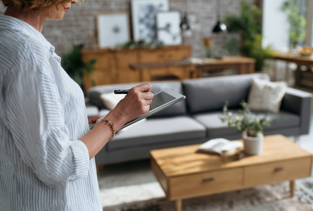 Eine Homestagerin steht mit einem Tablet in einem eingerichteten Wohnzimmer.