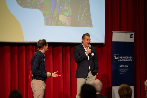Zwei Männer stehen mit Mikrofonen auf der Bühne des IVD West Kongress