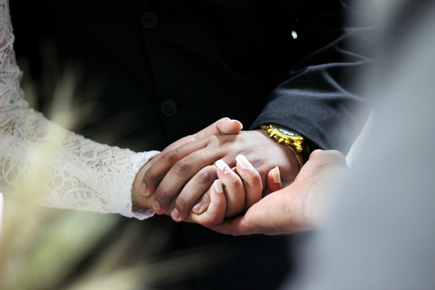 Ein Mann im Anzug und eine Frau im Hochzeitskleid halten sich an den Händen
