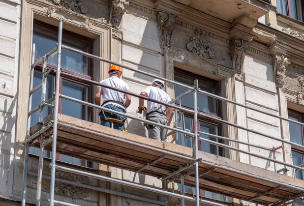 Zwei Bauarbeiter stehen auf einem Baugerüst vor einer Altbau-Fassade.