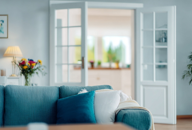 Eine Couch in einem Wohnzimmer, im Hintergrund sieht man die Tür zur Küche.