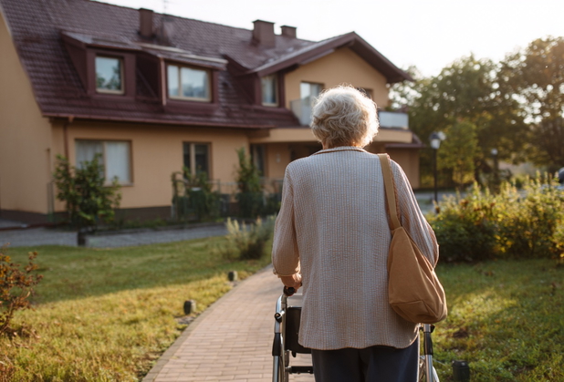 Eine alte Frau mit einem Rollator im Garten eines Pflegeheims.