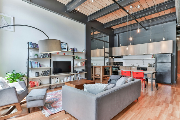 Ein modernes Wohnzimmer mit hoher Decke, in der Mitte des Raums eine graue Couch und ein Fernseher.