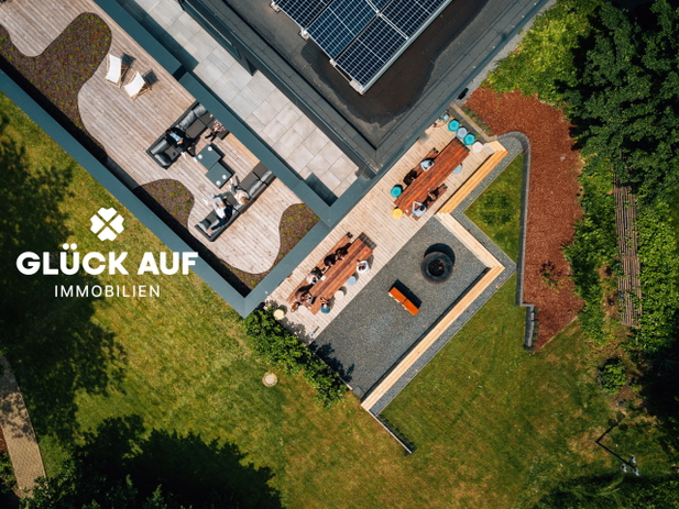 Vogelperspektive auf ein großes Wohnhaus mit Flachdach, großem Garten und Terrasse von Glück Auf Immobilien.