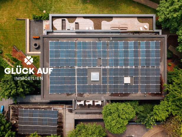 Vogelperspektive auf ein Haus mit Flachdach und vielen Solarpanels, drumherum Garten.