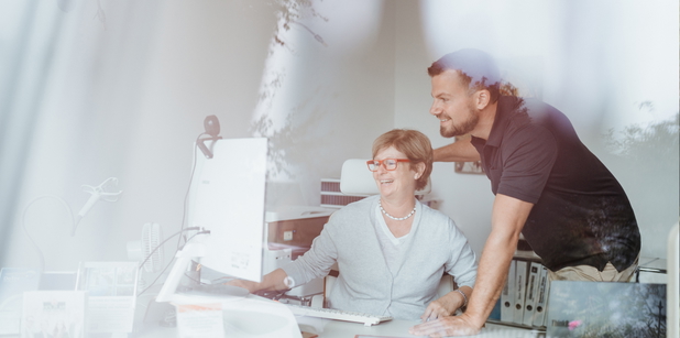 Zwei Mitarbeiter von Holzlar Immobilien am Schreibtisch vor dem Computer.