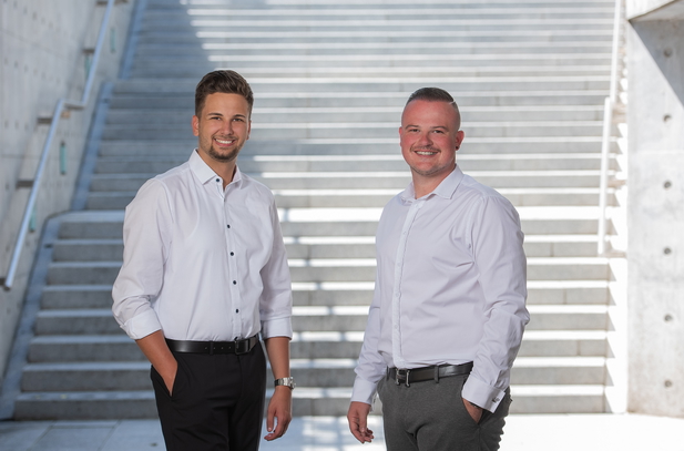 Killian Steinegger und Lars Schuster von Immobilienkanzlei Oberschwaben GmbH vor einer Treppe.
