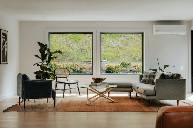 Ein Wohnzimmer mit Sofa und Sessel, im Hintergrund ein Fenster raus ins Grüne.
