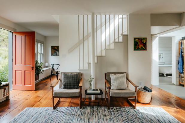 Ein Eingangsbereich, eine Treppe, ein Wohnzimmer und ein Teil eines Badezimmers in einem familiären Haus sind zu sehen.