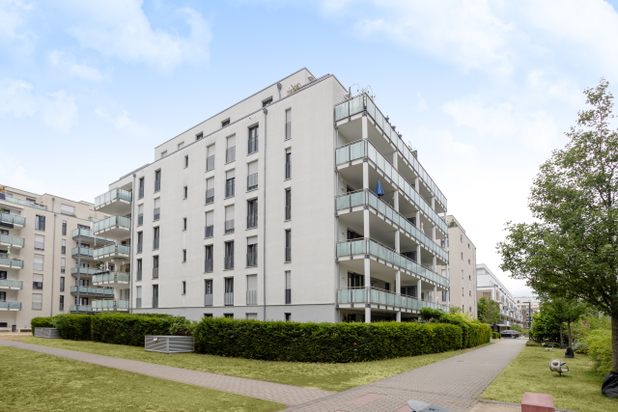 Großes weißes Gebäude mit mehreren Wohnungen umgeben von parkähnlicher Grünanlage.