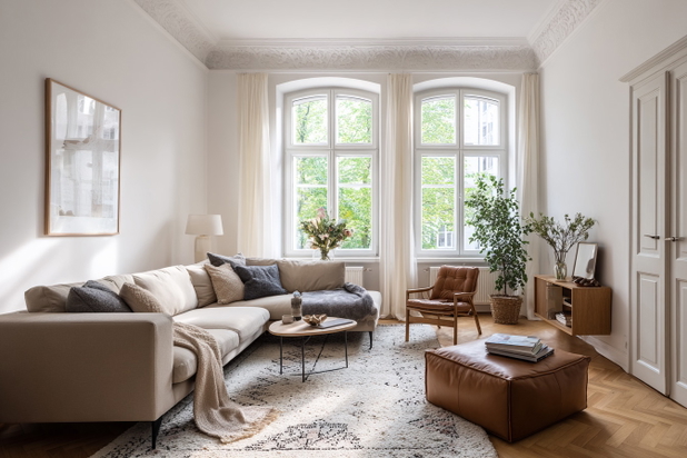 Gemütliches Wohnzimmer in einer Altbauwohnung mit großen Fenstern, Couch, Sessel und Dekoelementen.
