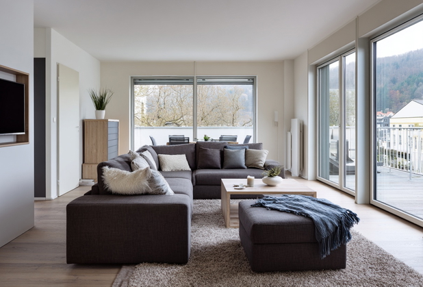 Ein Wohnzimmer mit einer braunen Couch, direkt vor einer Terasse mit schöner Aussicht.